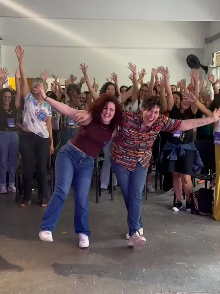 Pâmella e Agnes dançando diante das participantes com os braços levantados